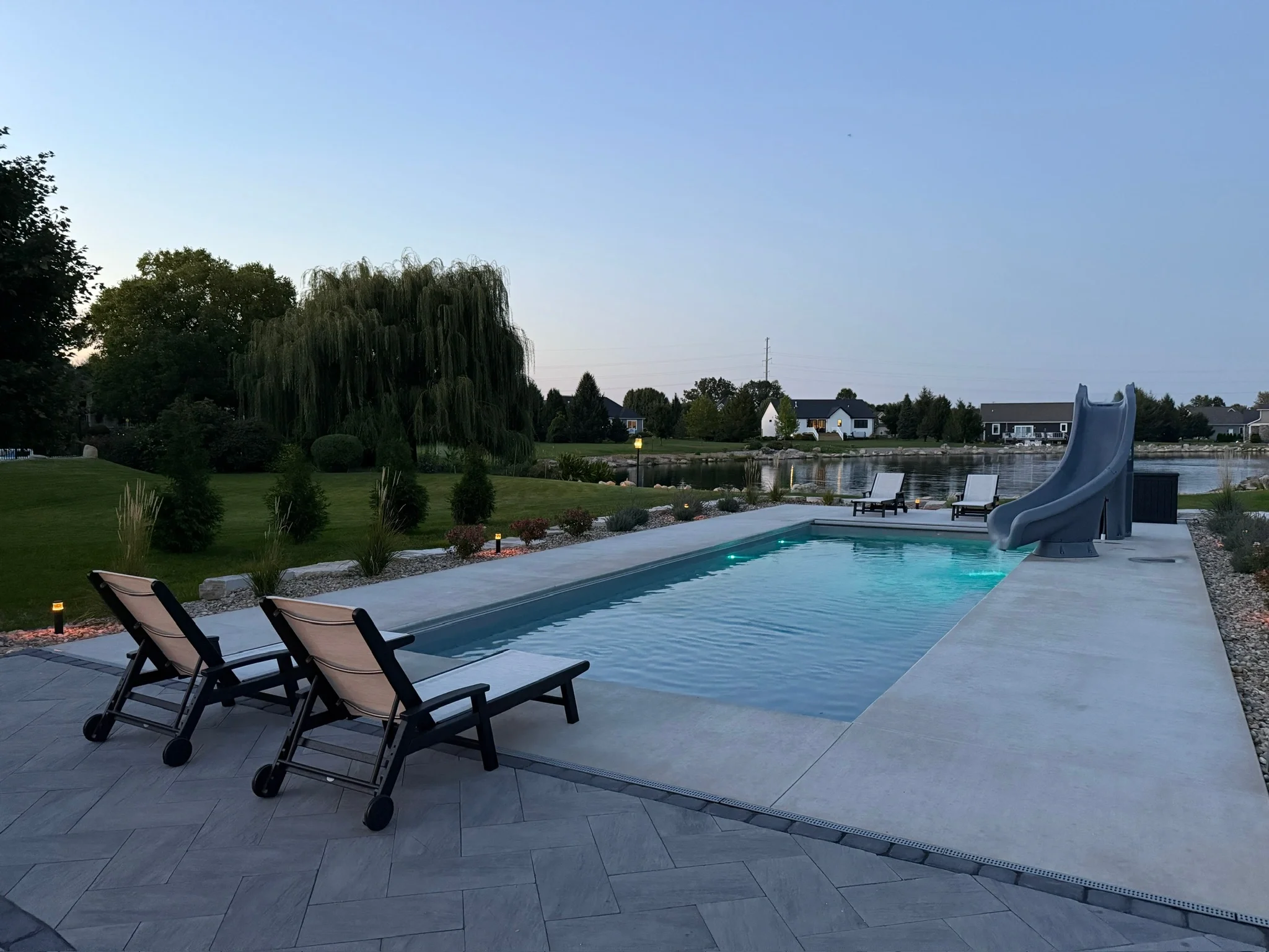 Pool with a slide and lounge chairs on a paver deck