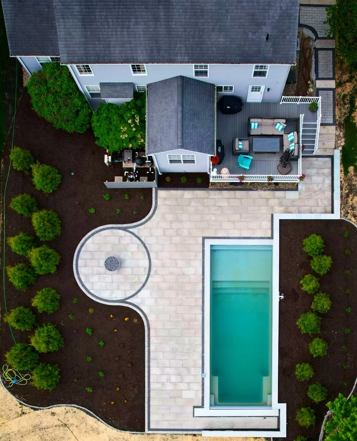 Aerial view of a narrow fiberglass pool and paver patio in a side yard