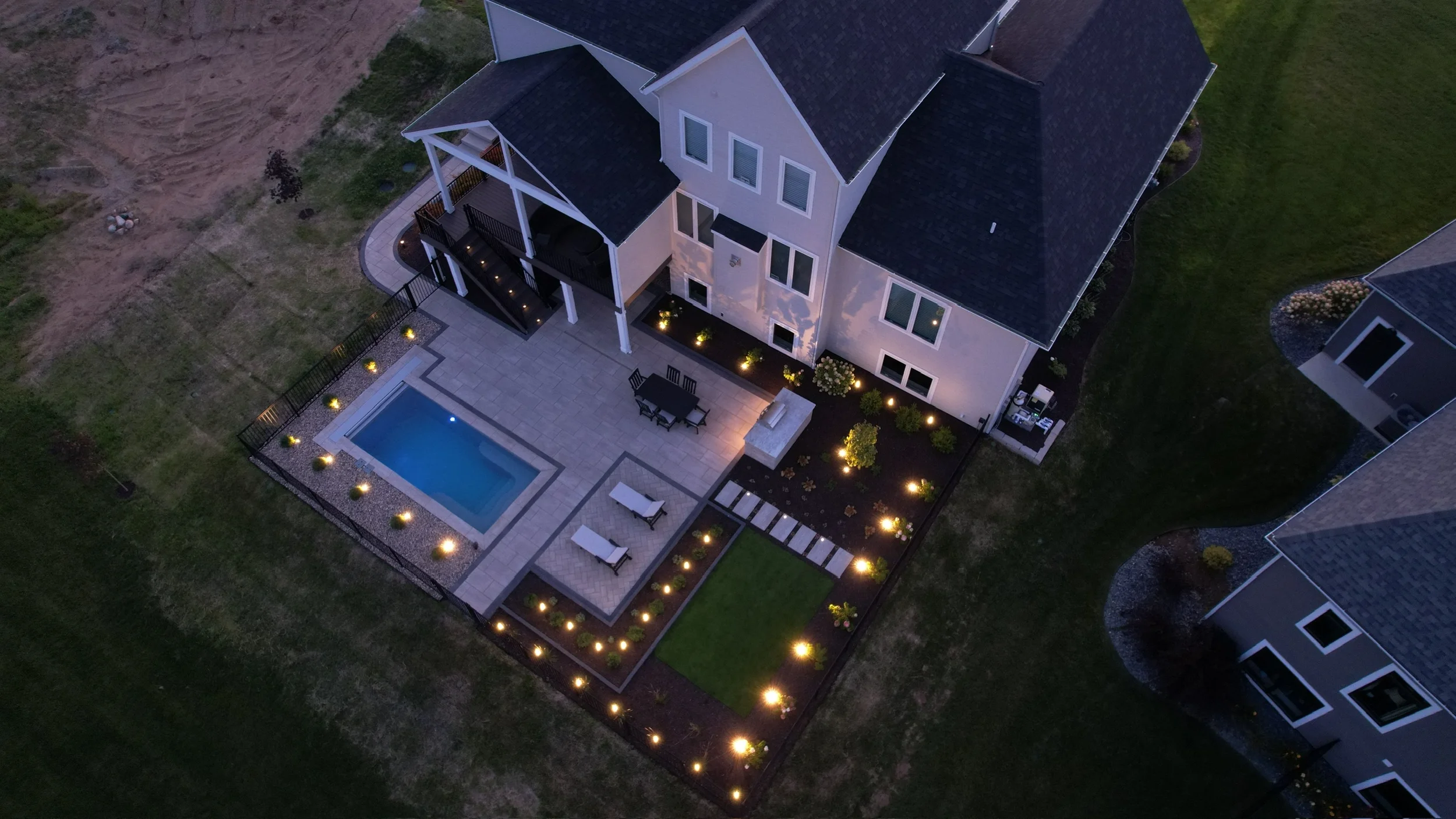 Aerial view of a lit backyard pool and patio at dusk