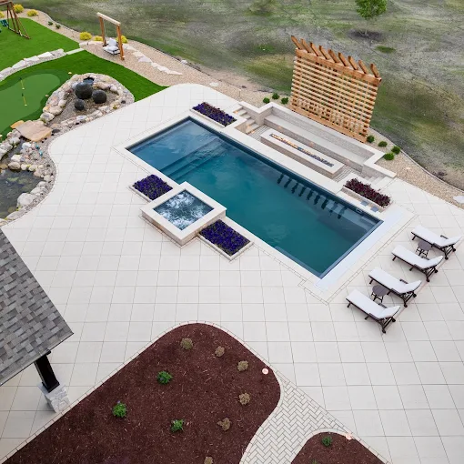 Aerial view of a pool with a spa and light paver deck